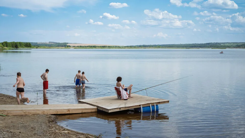 Okładka posta - przedstawia jezioro z wędkarzem i pływającymi dziećmi w gorący letni dzień